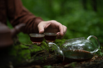 Man holding tea bowl of shu puer tea near glass cha hai in summer forest 