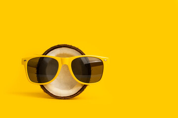 Coco fresco con gafas de sol sobre un fondo amarillo brillante liso y aislado. Vista de frente y de...
