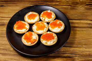 Tartlets with red caviar and soft cheese on a wooden table