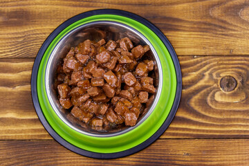 Canned food for cats or dogs in green metal bowl on wooden floor. Top view