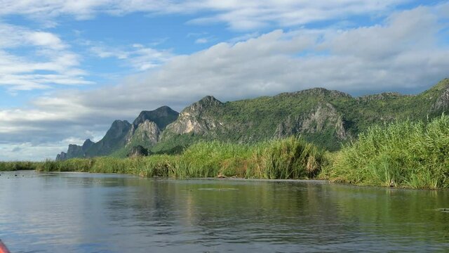Limestone mountain with rock cliff with green forest and reed field in lake , Traveling by boat on wetland with blue sky and white cloud in background at Khao Sam Roi Yot National Park, Thailand