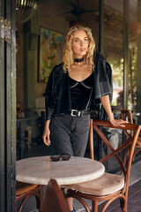 Woman Portrait. Beautiful Blonde Model In Fashionable Clothes. Sexy Female Resting Near Table And Chair In Cafe. Relaxation In Comfortable Restaurant.