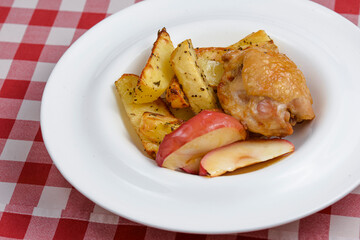Fried potatoes with meat and baked apples. Tasty dinner. Served in a white plate over red plaid tablecloth.