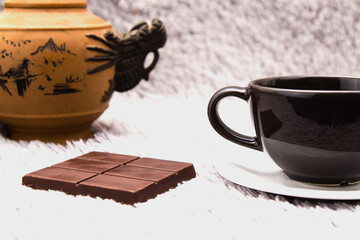 Chocolate and a Cup of tea on a grey background, with a teapot in the background.