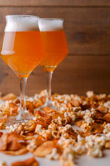 Two glass of beer and beer snacks over white and wooden background. Potato chips and salty popcorn.