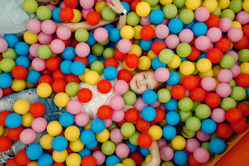Fototapeta na wymiar Girl lying among many colorful balls, playground