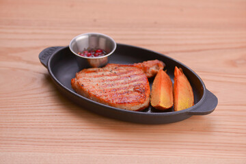 Rib eye steak served with baked potatoes and cranberry sauce on a black tray over light wooden background.