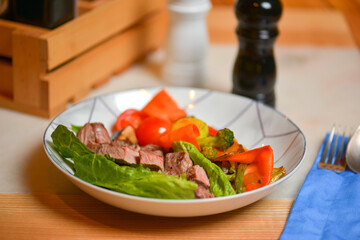 Salad with meat and vegetables. Italian cuisine, different dishes served in restaurant on light rustic wooden table.