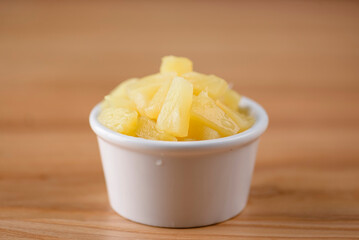 Pineapple chunks in the bowl isolated on wooden background. Snack, appetizer. Pizza ingredient.