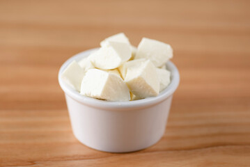 Cut cheese in a small white bowl. Snack, appetizer. Pizza ingredient.