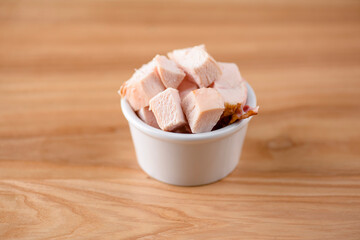 Bowl of cut ham in a small white bowl on wooden background. Snack, appetizer. Copy space banner. Pizza ingredient