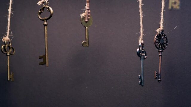 A lot of different old keys from different locks, hanging from the top on strings. Finding the right key, encryption, concept. Retro vintage brass keys on a dark background, low depth of field