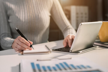 Female use tablet computer and take notes business documents in the notebook at the office desk in the morning.