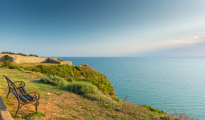 A bench on a coast at the sea shore during a summer sunset