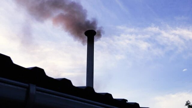 Metal pipe on roof of house with black smoke coming from it.