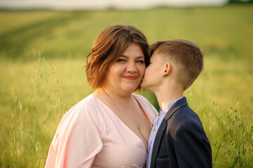 Mother and son in a green wheat field. Son kisses mother on the cheek.