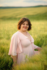 Portrait of a overweight woman in a pink dress. A woman is standing in a green wheat field.