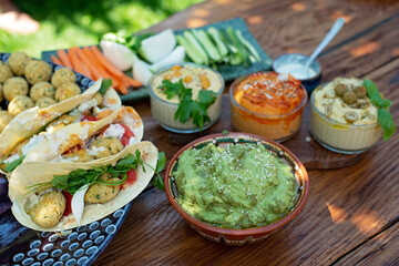 Vegetarian picnic on a wooden oak table, hummus, falafel, pita, vegetables, spinach, basil and sunflower seed pesto sauce. Healthy Mediterranean food.