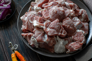 Raw mutton cut into medium pieces, lay on a plate, surrounded by red onions, a knife and chili peppers, tied with twine
