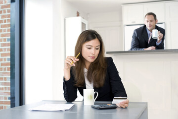 Businesswoman working out some calculations with businessman looking on