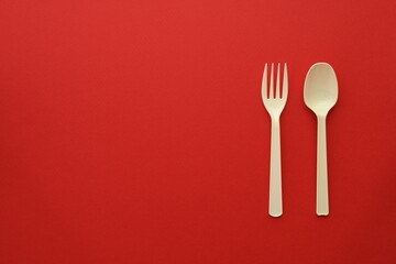 Plastic disposable fork and spoon on red background