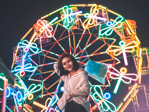 Portrait Of Woman Against Illuminated Ferris Wheel In Amusement Park At Night