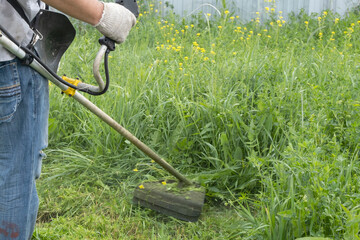 A man mows the thick tall grass with a gasoline trimmer. The lawn mower's work. High quality photo