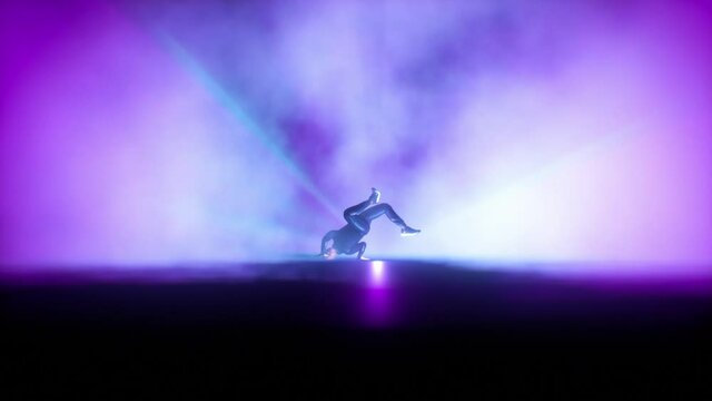 Break dancer dancing on a stage against colorful spotlights in slow motion