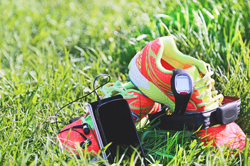 Sport watch, chest strap of a heart rate monitor, smartphone with headphone and sneakers on a grass background.