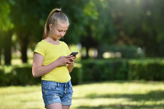 Young girl reads carefully the message in a smartphone on a background of green trees