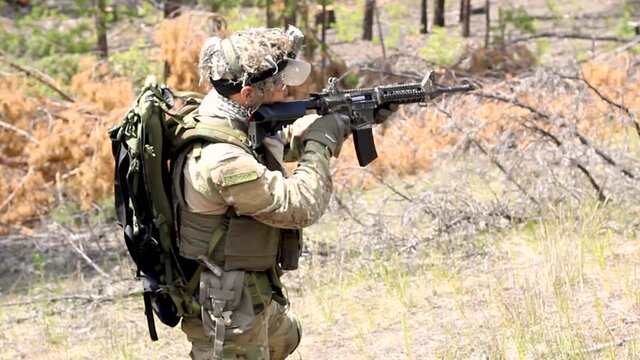 Fully armed american soldier on military range in active war game Airsoft shoots at the target