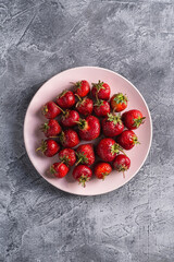 Fresh ripe strawberry fruits in pink plate, summer vitamin berries on grey stone background, top view