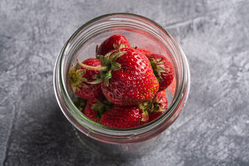 Fresh ripe strawberry fruits in glass jar, summer vitamin berries on grey stone background, angle view macro