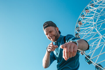 Happy young man in the city on a background of blue sky and ferris wheels. Space for text.