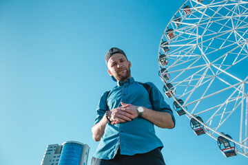 Young man in the city on a background of blue sky and ferris wheels. Space for text.
