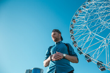 Young man in the city on a background of blue sky and ferris wheels. Space for text.