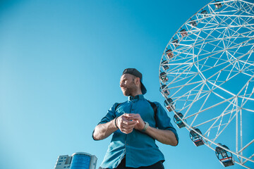 Young man in the city on a background of blue sky and ferris wheels. Space for text.