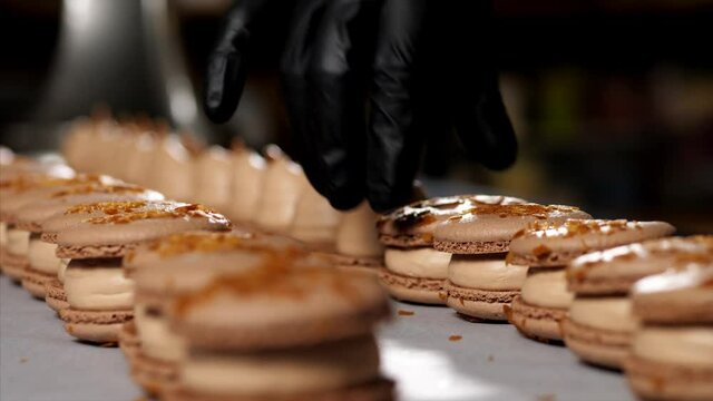 Chef is assembling caramel macarons. Close-up of hand in glove is puts a shells on french cookies.
