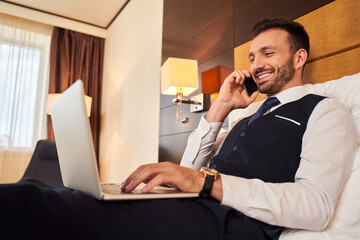 Smiling businessman using gadgets in hotel room