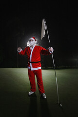 Man in Santa suit holding on to golf club and golf flag