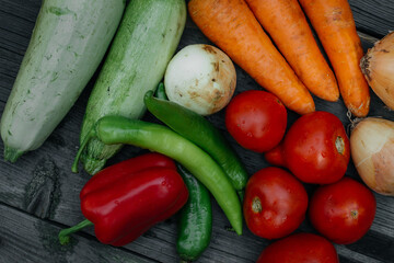 A variety of fresh vegetables, tomatoes, onions, zucchini, carrots, red and green peppers, on a rustic wooden table.