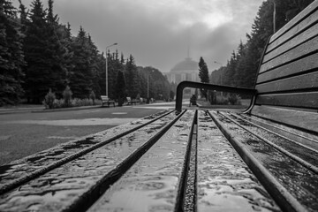 Selective focus on transparent drops of water on a bench in Victory Park on Poklonnaya Hill in Moscow. Blurred background. In the background is a memorial complex. Mainly cloudy. Black and white image