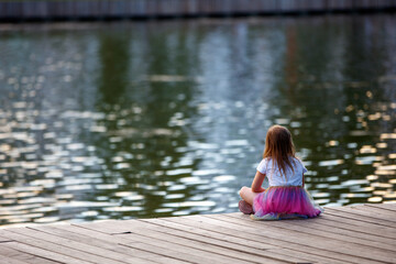A little girl sits on the bank of a pond