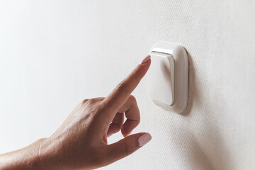 Female hand turns off the light indoors. Electrical energy saving