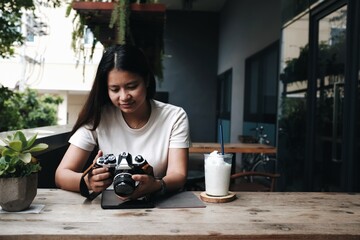 Asian woman sitting in a coffee shop taking a picture with a film camera