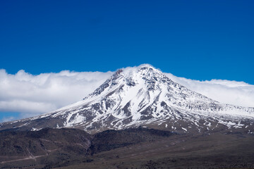 A snowy mountain peak, cloudy blue sky  