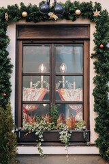 Fototapeta na wymiar Antique brown window decorated with Christmas branches of spruce with cones and toys. Lamps in the form of candles.The concept of festive decor in the exterior.