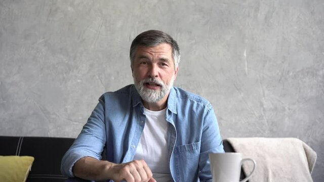 Serious senior old grandfather talking looking at camera at home, elder man online teacher blogger sit on sofa communicating by webcam in distance conference video call recording vlog, webcamera view.
