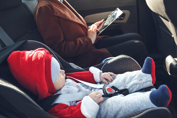 Mother with her small child in a baby car seat ride in the back seat of a taxi