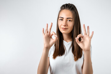 Good job! Pretty carefree modern stylish European girl with long chestnut hair making OK with both hands, gesture as if saying that everything is finee, white background